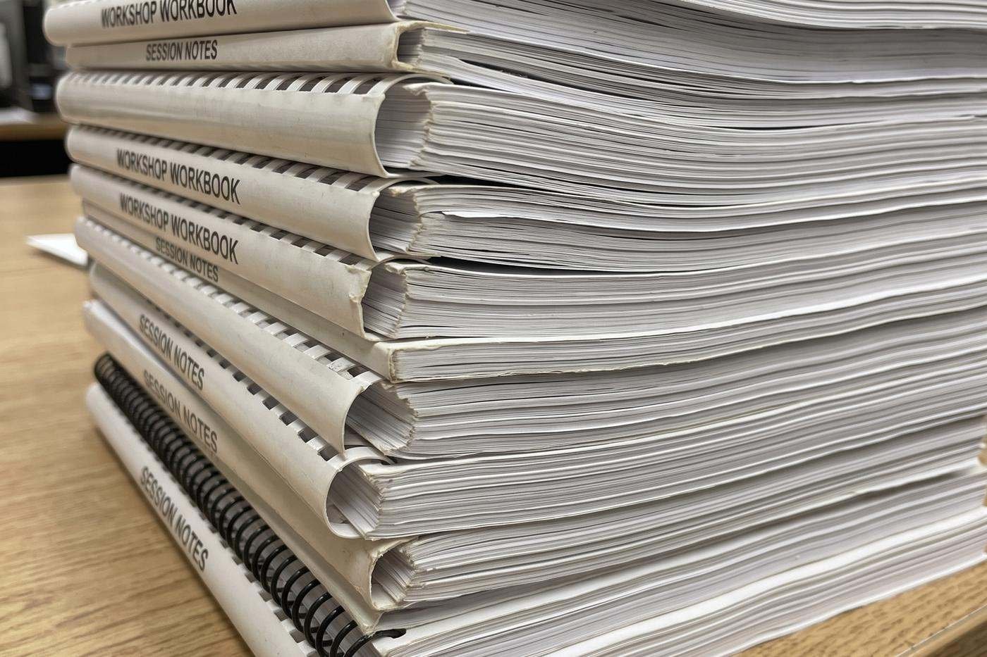 A stack of comb-bound workbooks and session notes on a desk, edges worn from use.